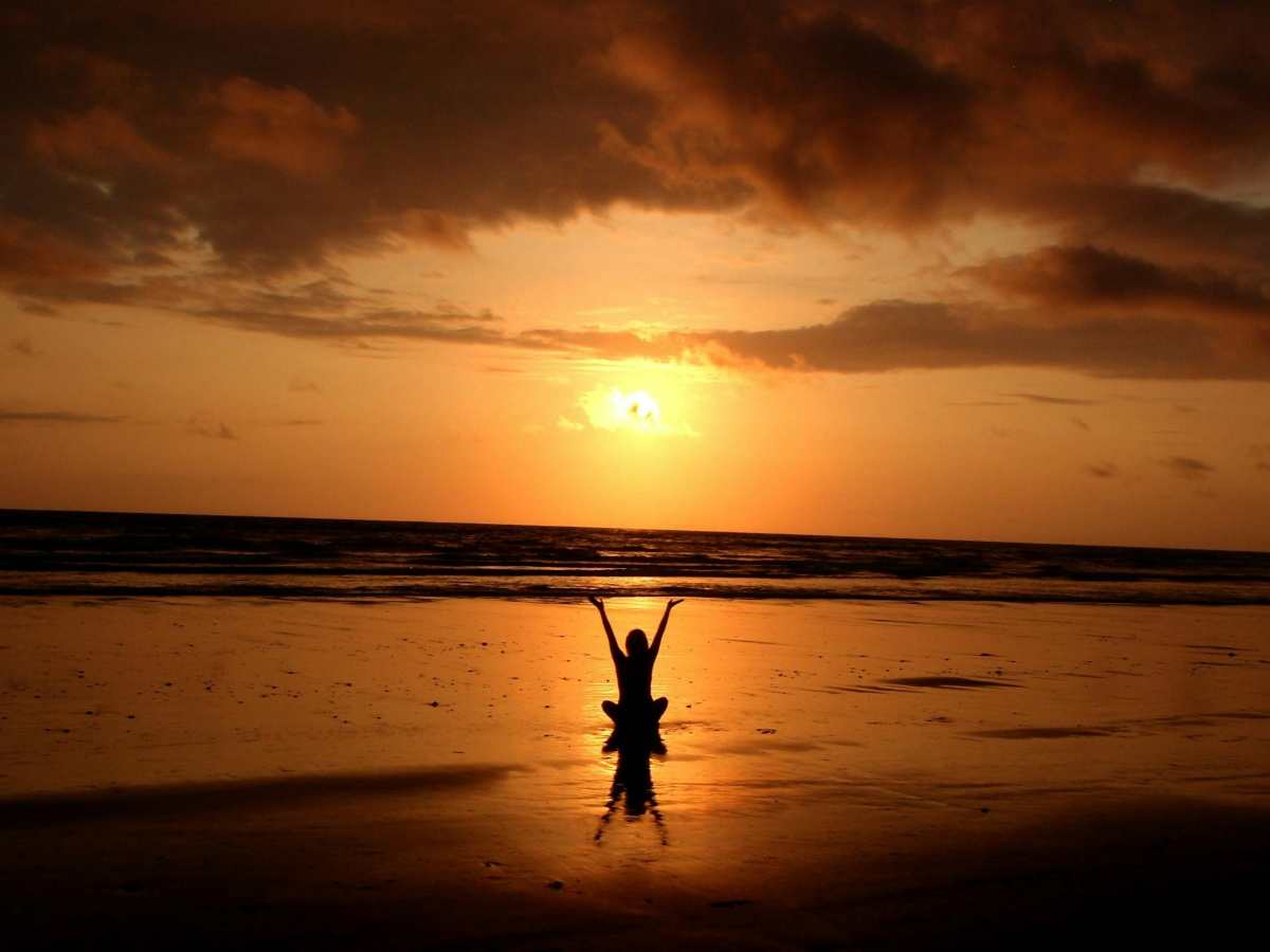 Person meditating on a beach at sunset, symbolizing mindfulness and calm in CBT practice