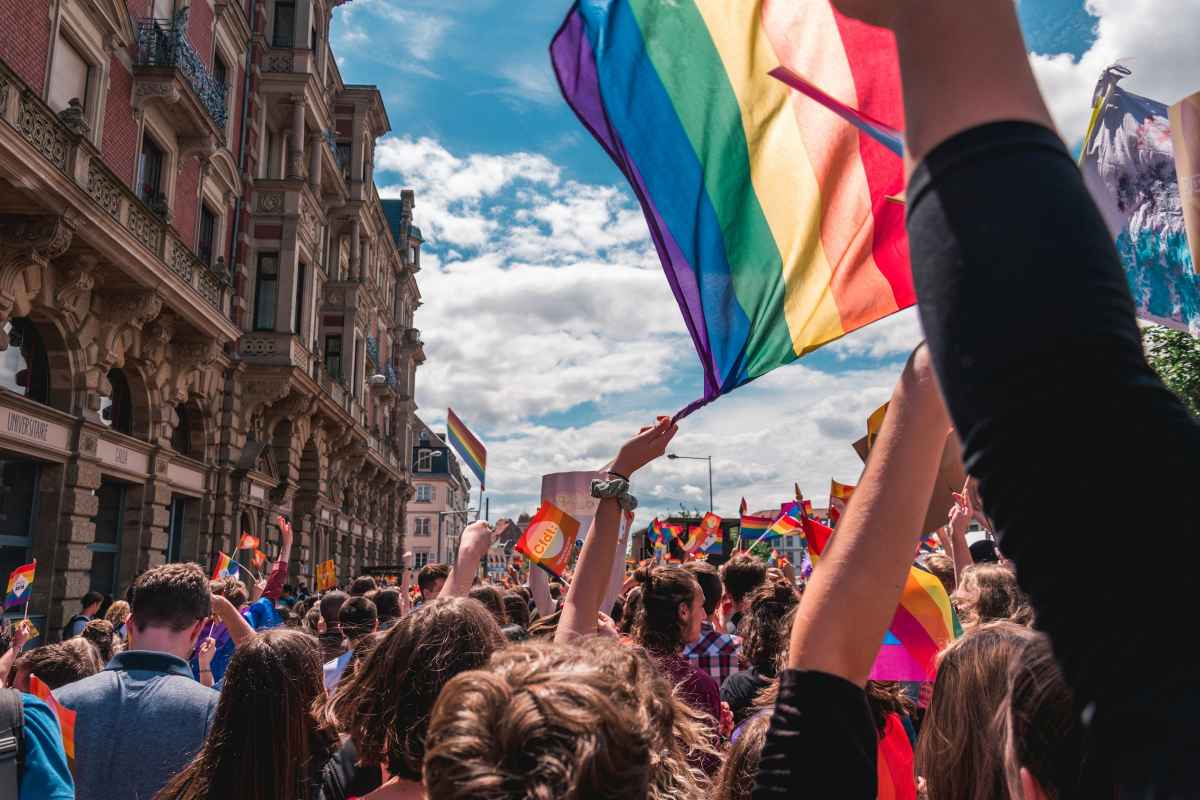 A large crowd waving rainbow flags during a Pride march, symbolizing LGBTQ community, resilience, and collective experiences of trauma and healing.