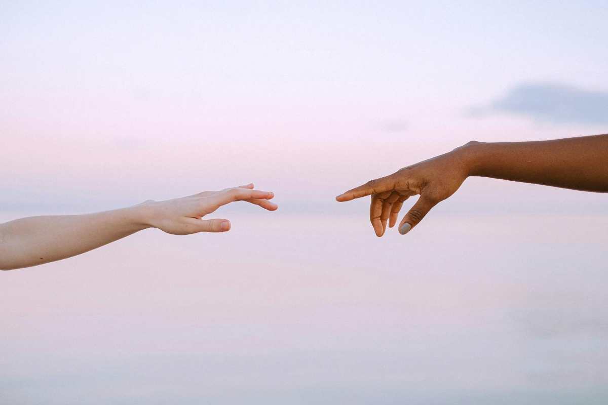 Two hands reaching toward each other against a soft sky, symbolizing connection, healing, and shared humanity in liberation psychology.